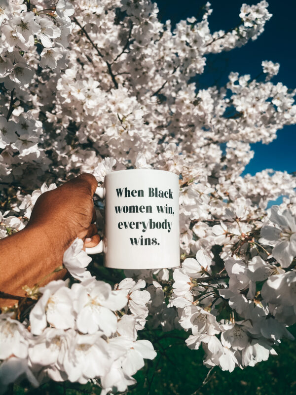 When Black Women Win Everybody Wins mug being held by the handle in a cherry blossom tree
